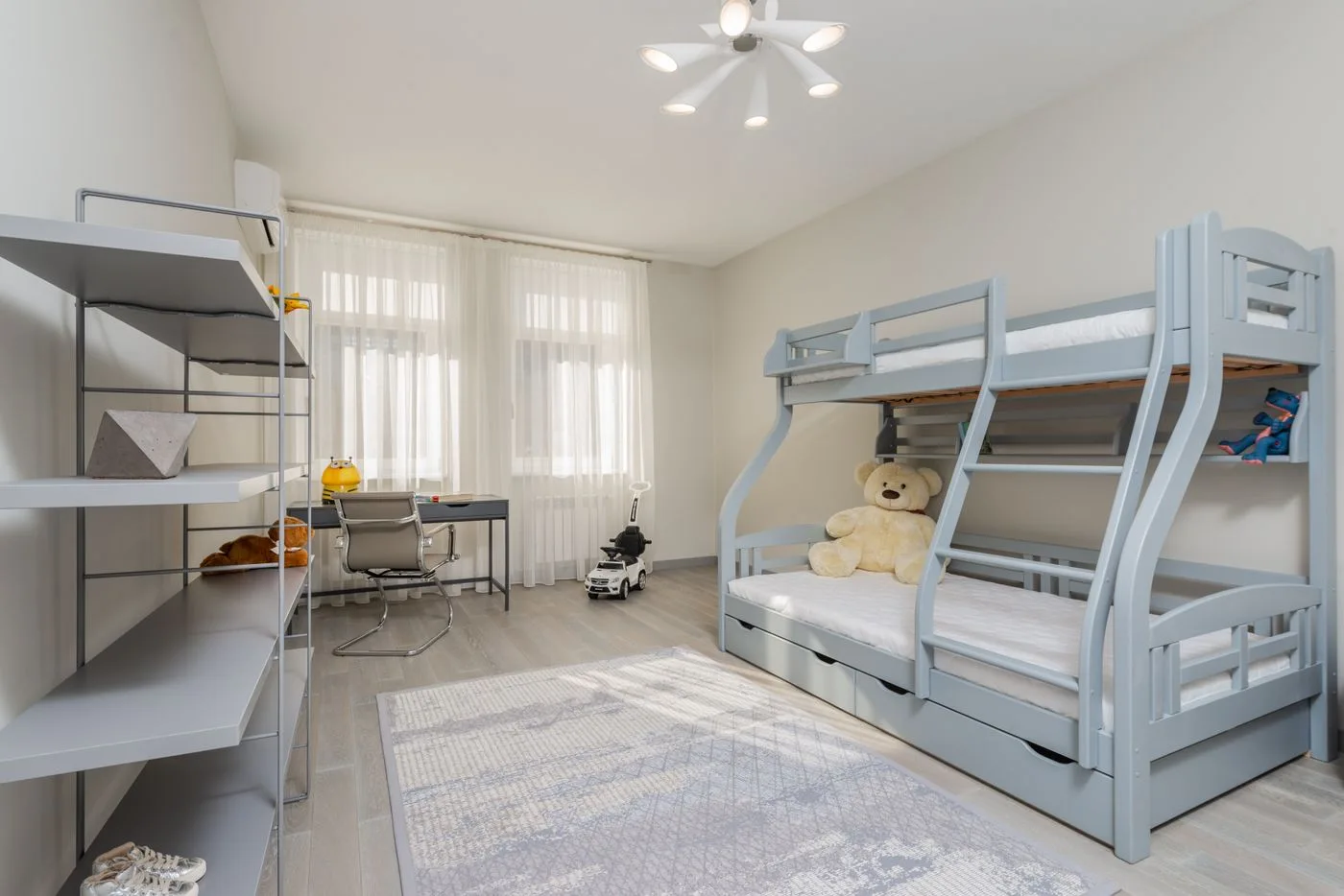 A children's room with bunk beds, shelves and a desk