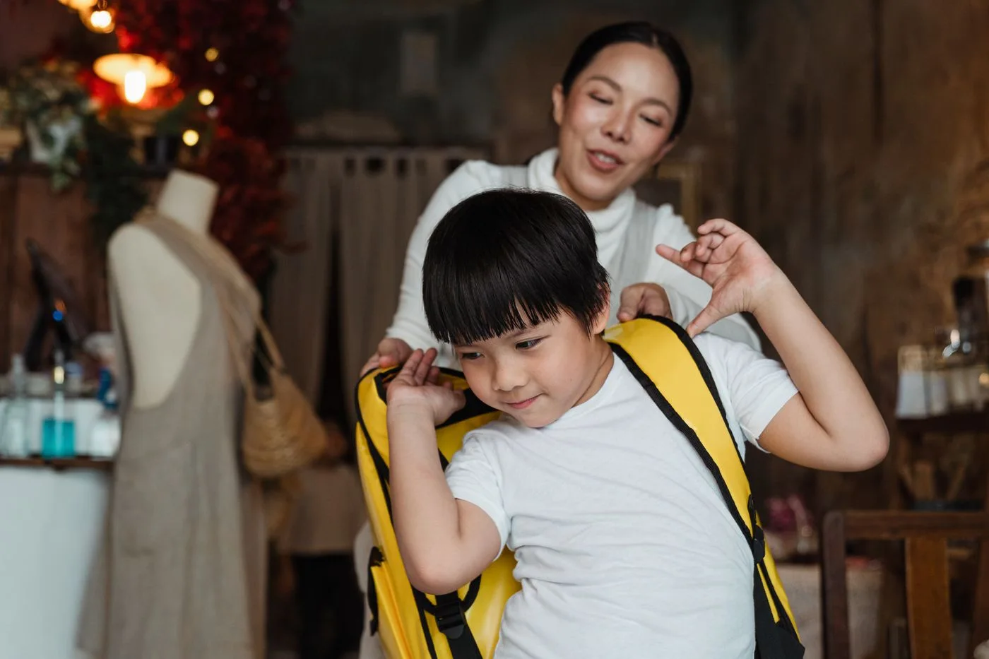 A mother helping a child put on a yellow backpack